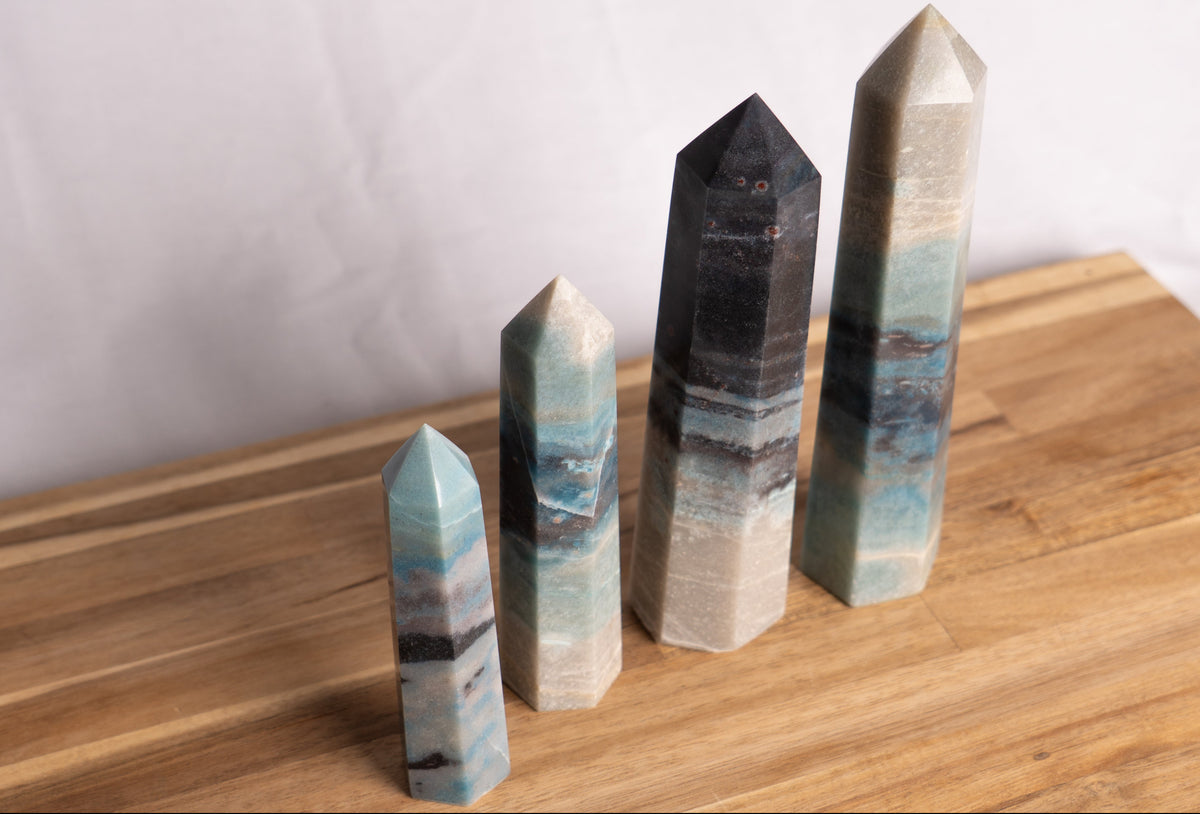 Four polished crystal points of varying heights arranged on a wooden board against a light gray backdrop.